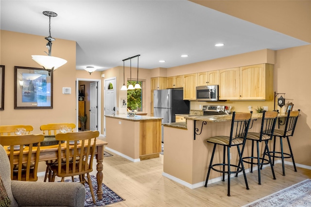 1750 E Lakeshore Dr Unit 212, Whitefish, MT 59937 - kitchen featuring appliances with stainless steel finishes, light brown cabinets, a peninsula, light wood-style flooring, and light stone counters