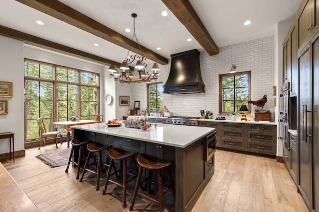176 Whitefish Hills Loop, Whitefish, MT 59937 - kitchen featuring custom exhaust hood, light countertops, light wood-style floors, beam ceiling, and a breakfast bar area