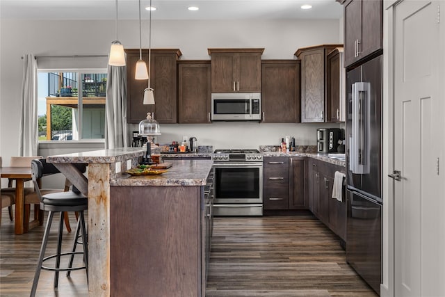 6910 Shaver Dr, Missoula, MT 59803 - kitchen with appliances with stainless steel finishes, dark brown cabinetry, dark wood finished floors, a breakfast bar, and a kitchen island