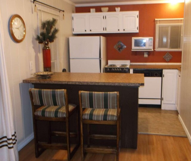 905 3rd Ave E, Kalispell, MT 59901 - kitchen featuring white appliances, white cabinetry, a peninsula, wood finished floors, and a breakfast bar