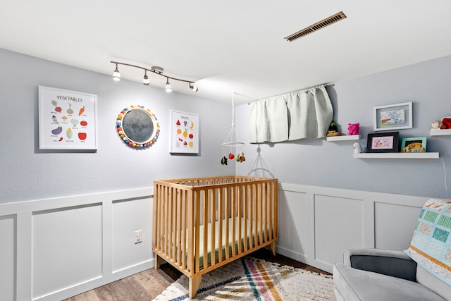 2604 5th Ave S, Great Falls, MT 59405 - bedroom featuring a decorative wall, a nursery area, wood finished floors, a wainscoted wall, and track lighting