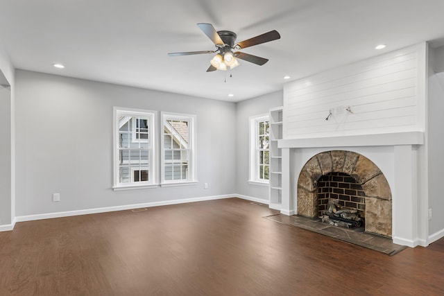 unfurnished living room featuring dark hardwood / wood-style floors, a stone fireplace, and ceiling fan