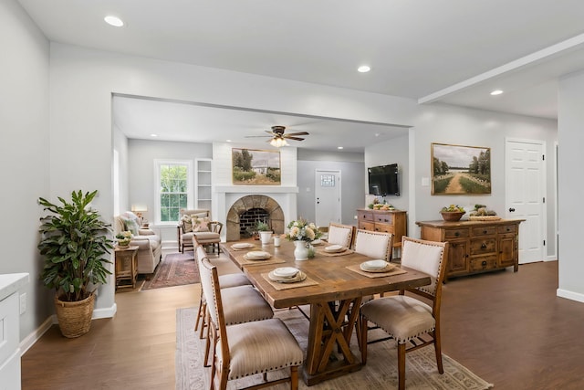 dining area featuring a large fireplace, dark hardwood / wood-style floors, and ceiling fan