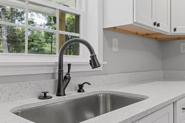 interior details featuring white cabinetry, light stone counters, and sink