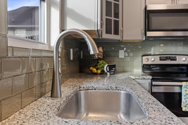 kitchen with stainless steel appliances, light stone countertops, sink, and backsplash