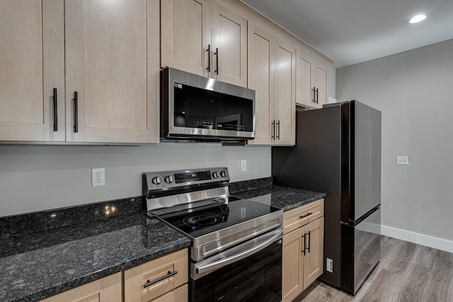 kitchen with stainless steel appliances, light brown cabinetry, light hardwood / wood-style flooring, and dark stone countertops