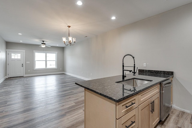 kitchen with light brown cabinetry, an island with sink, sink, dark stone counters, and light hardwood / wood-style flooring