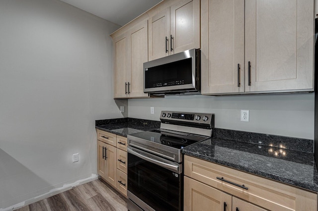 kitchen with stainless steel appliances, light hardwood / wood-style flooring, light brown cabinets, and dark stone counters