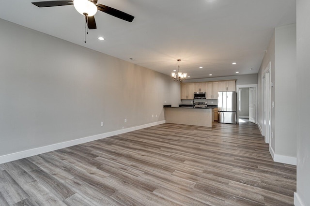 unfurnished living room featuring ceiling fan with notable chandelier and light hardwood / wood-style flooring