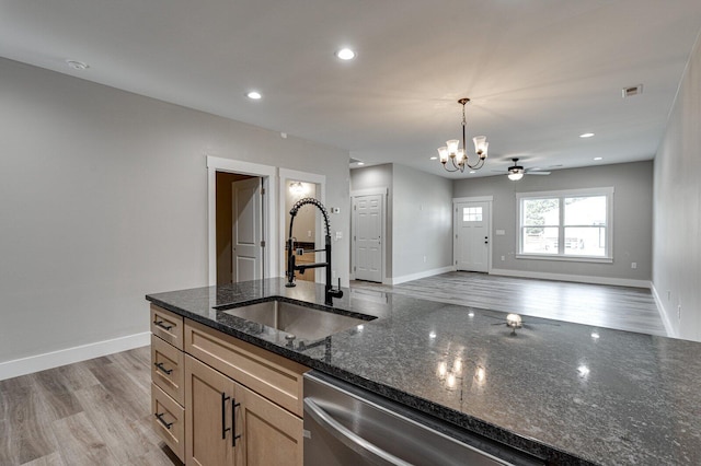 kitchen featuring pendant lighting, sink, dishwasher, dark stone counters, and light wood-type flooring