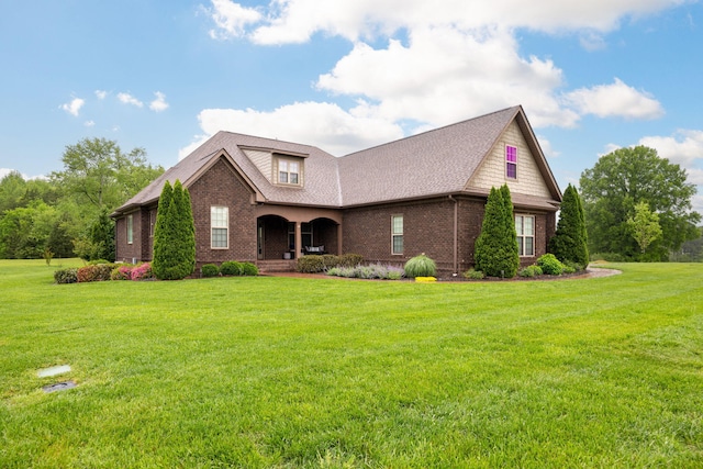 view of front of home with a front yard, a shingled roof, covered porch, and brick siding