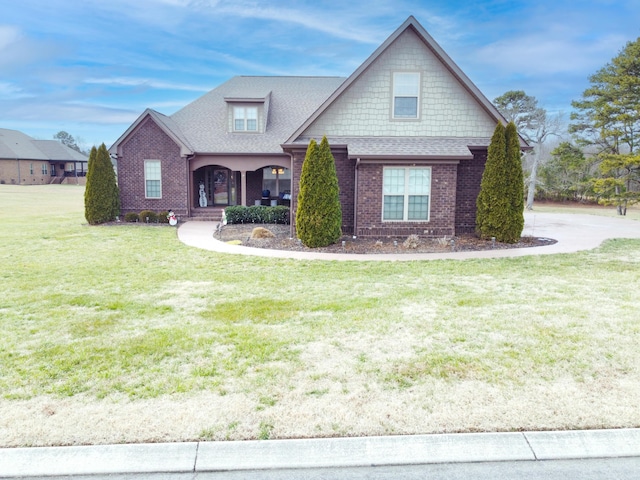 craftsman house with roof with shingles, a porch, a front lawn, and brick siding