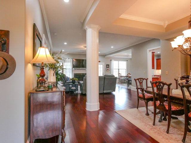 foyer featuring a chandelier, a fireplace, ornamental molding, dark wood-style floors, and ornate columns