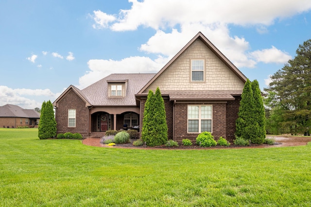 craftsman-style house with a front lawn, a shingled roof, covered porch, and brick siding