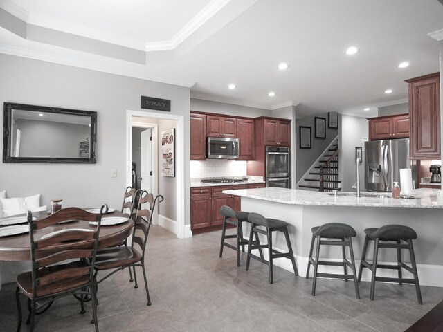 kitchen with ornamental molding, appliances with stainless steel finishes, backsplash, and a kitchen bar