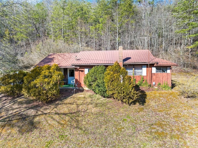 single story home featuring a front lawn, a standing seam roof, a forest view, metal roof, and a chimney