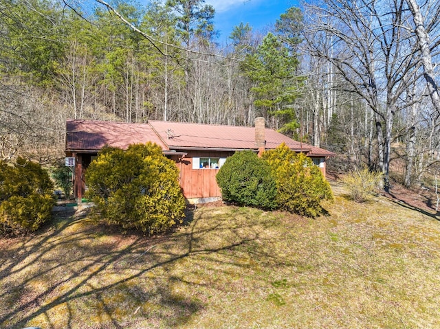 exterior space featuring a forest view, metal roof, and a yard