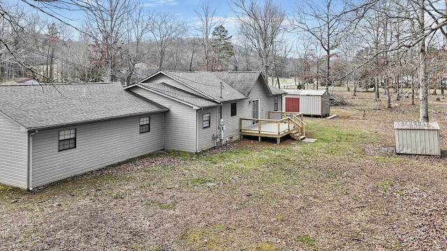 back of property featuring a wooden deck, a shingled roof, a storage shed, and an outdoor structure