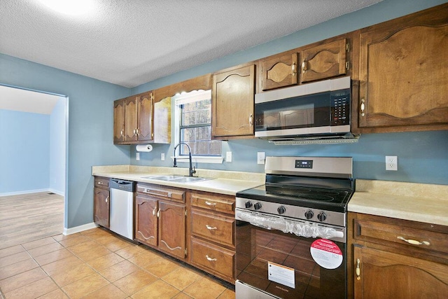 kitchen with a sink, appliances with stainless steel finishes, light countertops, light tile patterned floors, and baseboards