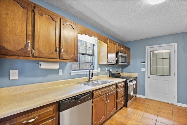 kitchen with brown cabinets, a sink, stainless steel appliances, light countertops, and light tile patterned floors