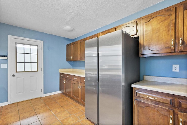 kitchen with light countertops, light tile patterned floors, freestanding refrigerator, and a textured ceiling