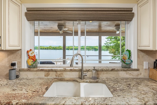 kitchen with light stone countertops, sink, tasteful backsplash, cream cabinets, and a water view