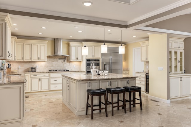 kitchen featuring a center island with sink, sink, wall chimney exhaust hood, appliances with stainless steel finishes, and a breakfast bar area