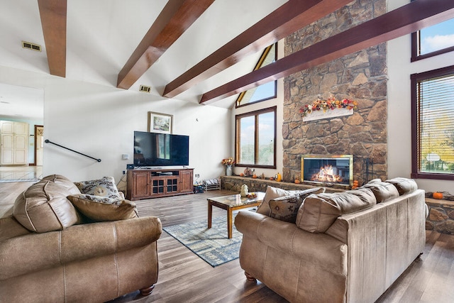 living room with a stone fireplace, hardwood / wood-style floors, beamed ceiling, and a high ceiling