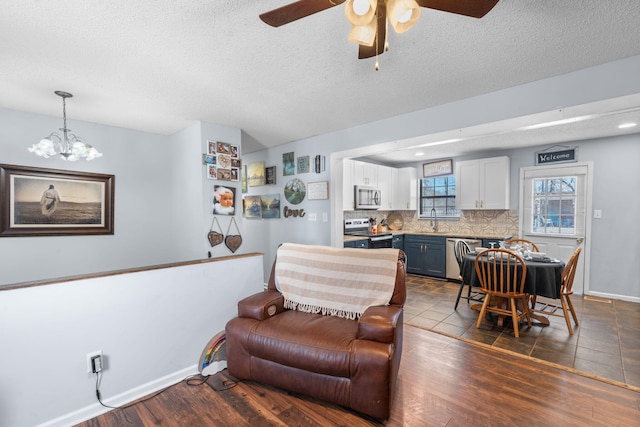 living room with baseboards, dark wood finished floors, a textured ceiling, and ceiling fan with notable chandelier