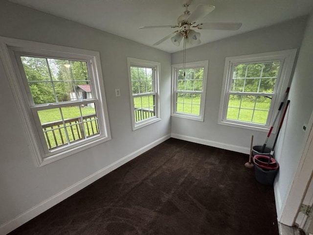 interior space featuring baseboards, a ceiling fan, and dark carpet