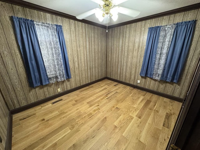 unfurnished room featuring visible vents, wood walls, baseboards, ceiling fan, and light wood-style flooring