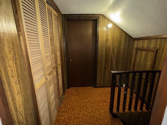 hallway featuring wooden walls, carpet floors, a textured ceiling, an upstairs landing, and vaulted ceiling