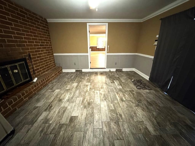 unfurnished living room featuring a wainscoted wall, ornamental molding, a brick fireplace, and wood finished floors