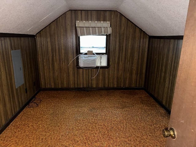 additional living space featuring electric panel, vaulted ceiling, wood walls, and a textured ceiling