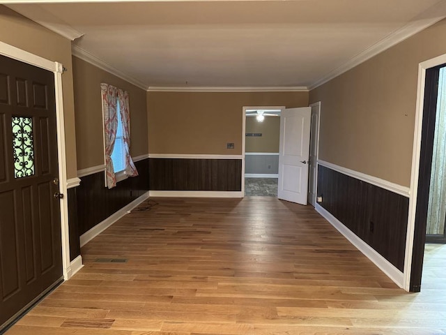 foyer with ornamental molding, a wainscoted wall, and light wood-style floors