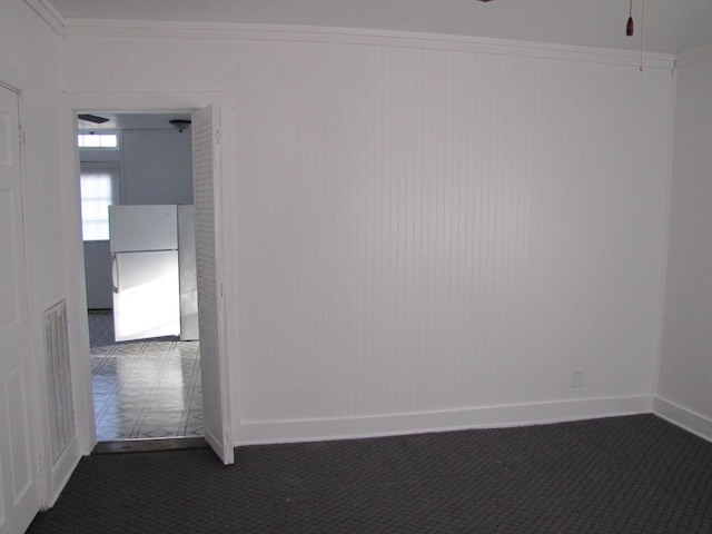 spare room featuring baseboards, visible vents, dark carpet, and crown molding