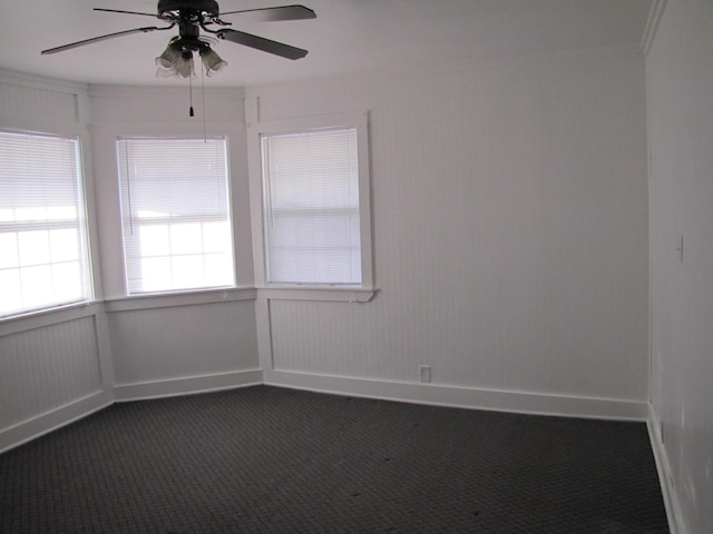 empty room featuring dark colored carpet, a ceiling fan, and baseboards