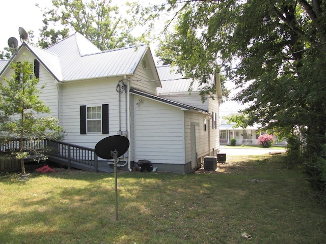 view of side of home with central air condition unit, a deck, metal roof, and a lawn