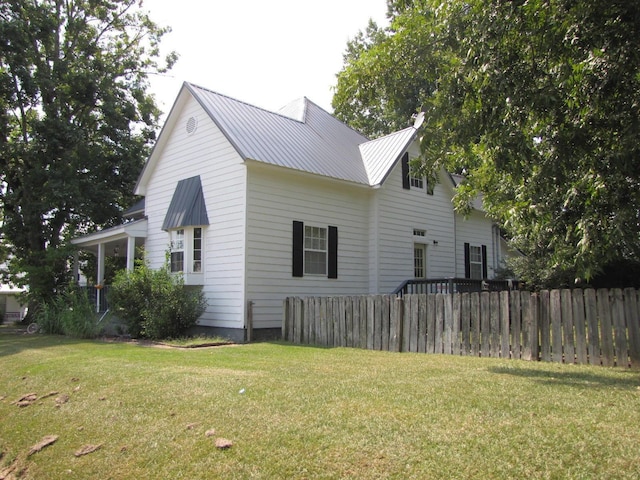 view of side of property with fence, metal roof, and a lawn