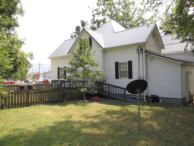 rear view of property with metal roof, a lawn, a wooden deck, and fence