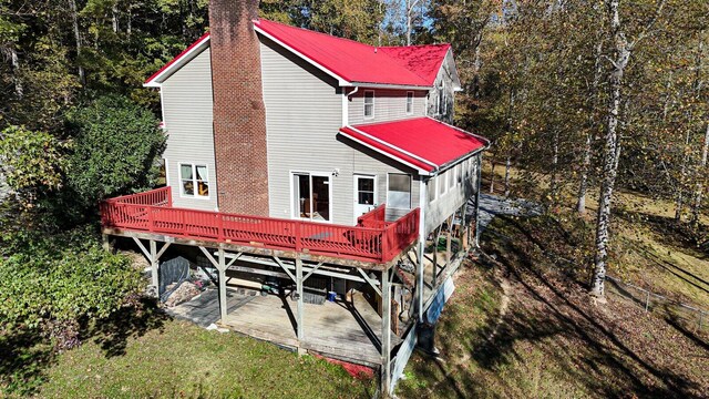 rear view of property with a chimney, a wooden deck, metal roof, a patio, and a yard