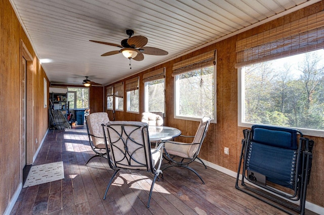 sunroom featuring baseboards, a wooden deck, wood walls, and wood-type flooring