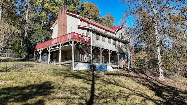 rear view of property featuring a chimney, a deck, fence, and a lawn