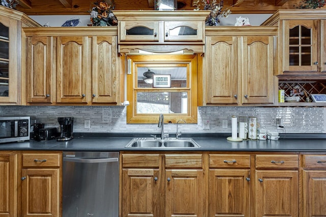 kitchen with decorative backsplash, dark countertops, appliances with stainless steel finishes, glass insert cabinets, and a sink