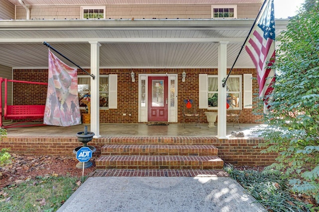 view of exterior entry featuring covered porch and brick siding