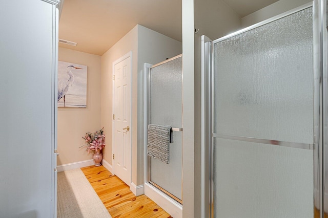bathroom with a stall shower, baseboards, visible vents, and wood finished floors