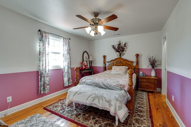 bedroom featuring baseboards, ceiling fan, visible vents, and wood finished floors
