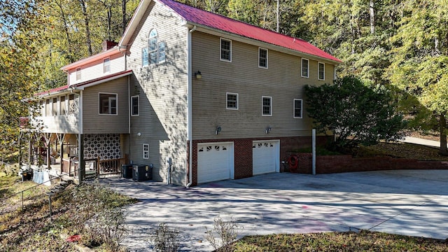 view of home's exterior with metal roof, driveway, central AC unit, a garage, and a chimney