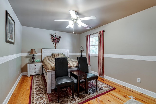 bedroom featuring a ceiling fan, visible vents, baseboards, and wood finished floors