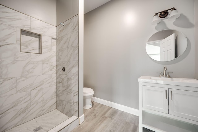 bathroom with vanity, toilet, a tile shower, and wood-type flooring